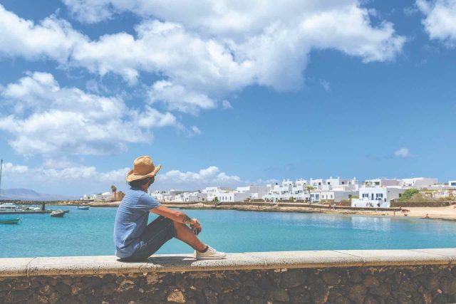 Man sitting on wall looking towards Caleta de Sebo, La Graciosa, Canary Islands, Spain