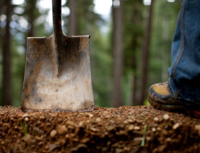 Pala conficcata nel terreno e stivali da trail: simbolo del lavoro sui sentieri per la storia sugli spot MTB