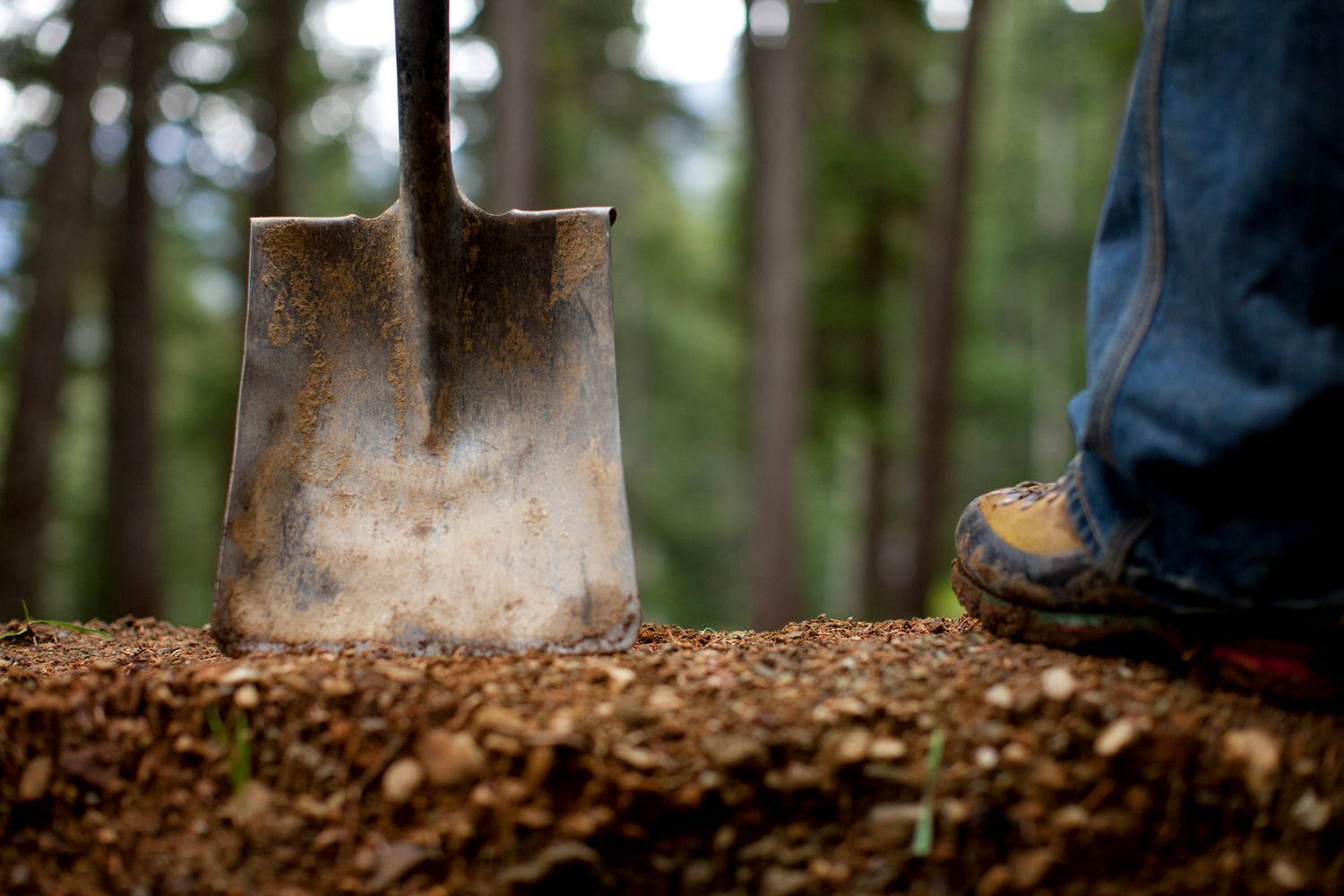 Pala conficcata nel terreno e stivali da trail: simbolo del lavoro sui sentieri per la storia sugli spot MTB