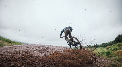 Mountain biker che affronta un trail bagnato, con fango e pioggia che evidenziano le condizioni tecniche