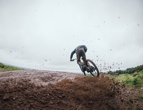 Mountain biker che affronta un trail bagnato, con fango e pioggia che evidenziano le condizioni tecniche