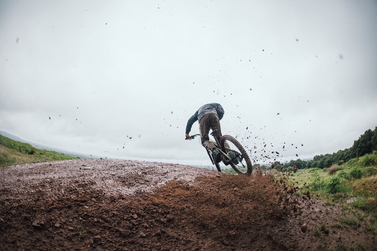 Mountain biker che affronta un trail bagnato, con fango e pioggia che evidenziano le condizioni tecniche