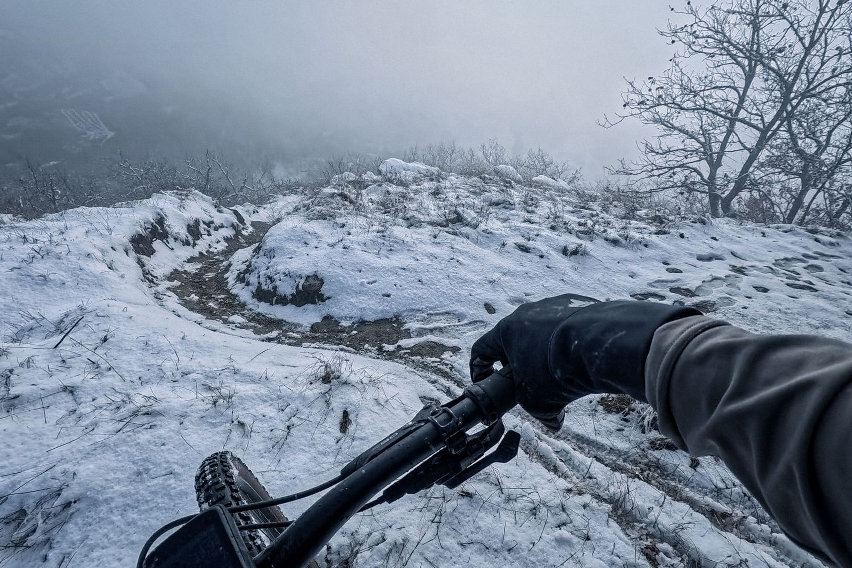 Visuale dal manubrio su sentiero innevato e scivoloso, tra alberi spogli e nebbia